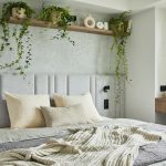 Stylish bedroom interior in modern apartment with small bed, wooden chest, home garden, white bedding, pillows and blanket. Sunny space with grey walls and brown wooden parquet. Template
